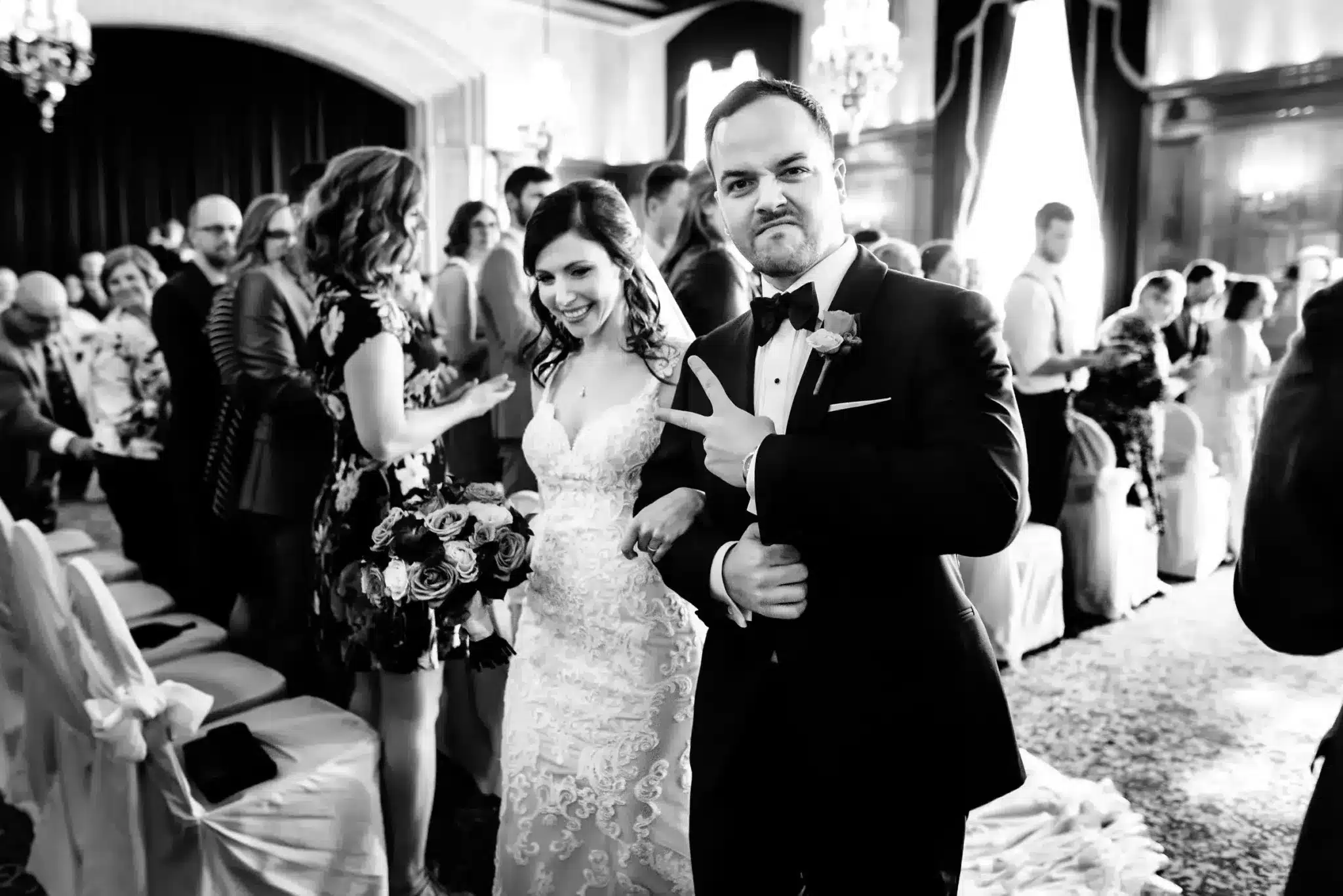 Winnipeg Wedding Photographer capturing groom giving peace sign while walking down the aisle with his bride.